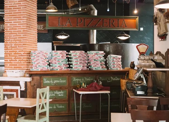 Balcão de pizzaria com caixas de pizza e forno ao fundo